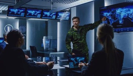 Picture of a military National Guard pointing to a screen of a map of the world to a group of men and a woman